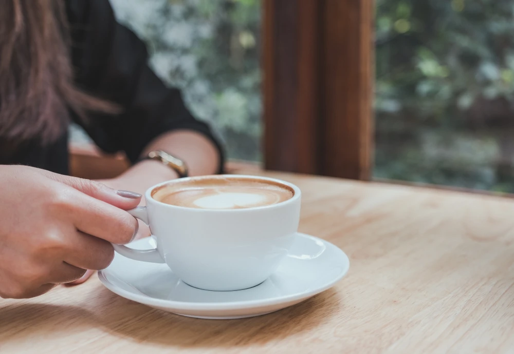 Woman holding cup of cappuccino at wooden table.