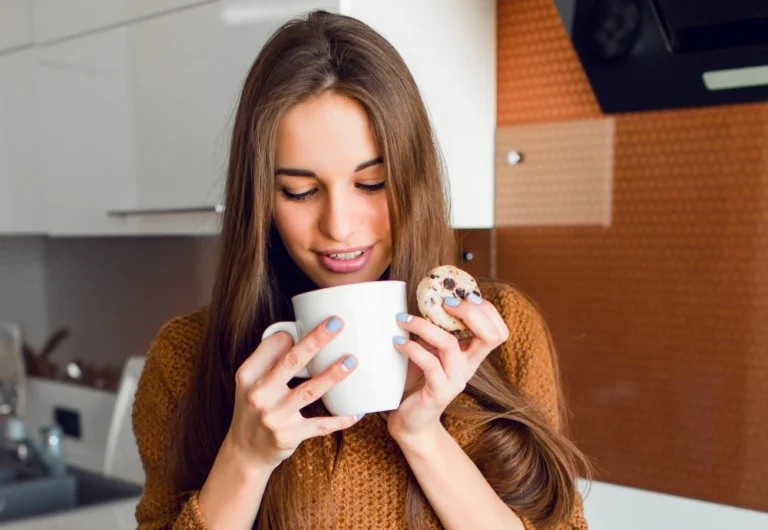 Woman enjoying coffee and cookie in kitchen.