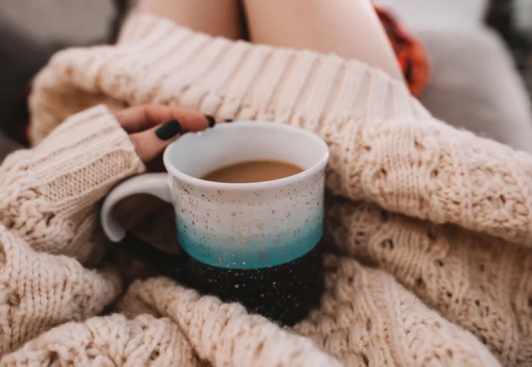 Person holding coffee mug in cozy knitted sweater.