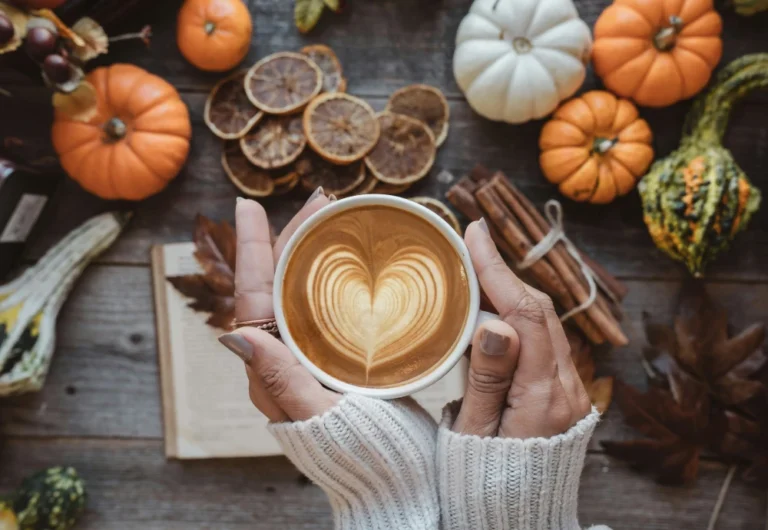 Hands holding latte amidst autumn decorations.