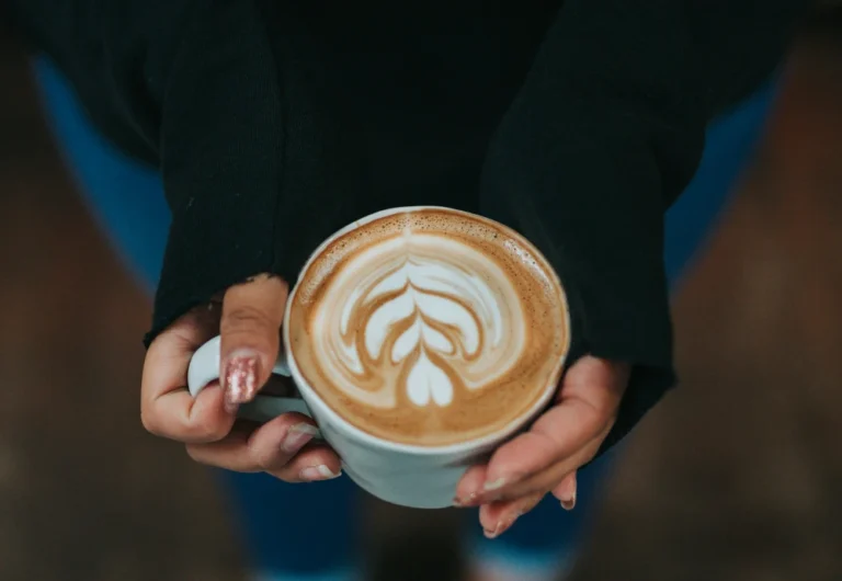 Person holding cup of latte with intricate foam art.