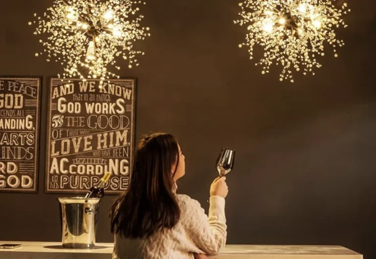 Woman admiring chandelier while holding wine glass.