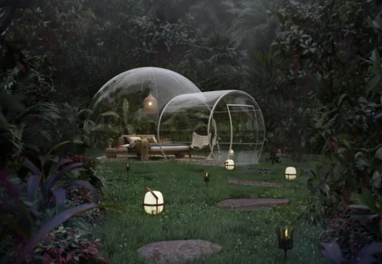 Transparent dome lounges in lush, foggy garden at dusk.