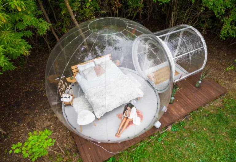 Transparent garden bubble tent with relaxed woman inside.