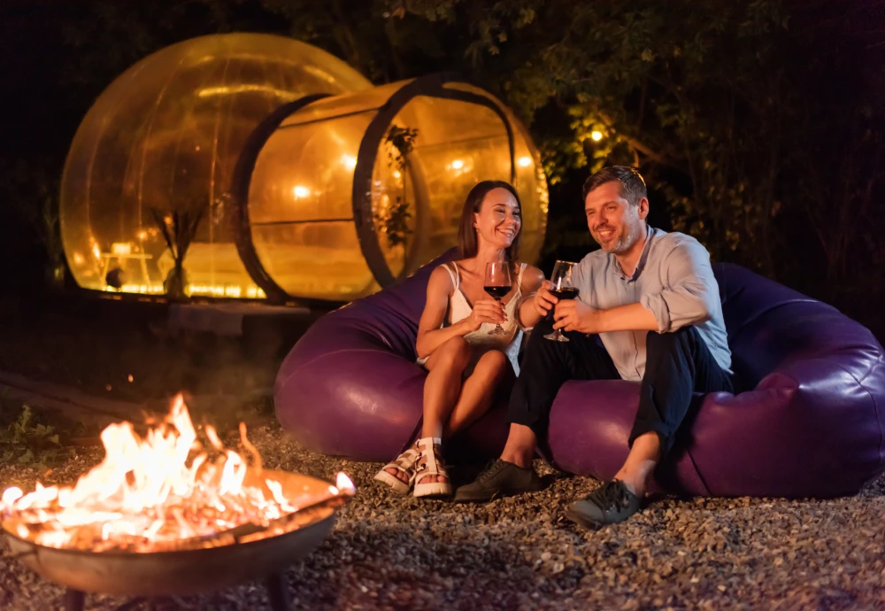 Couple enjoying wine by fire near glowing outdoor pod.