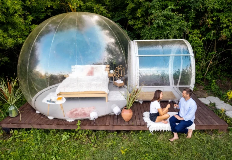 Couple at outdoor bubble hotel with bed and wine.