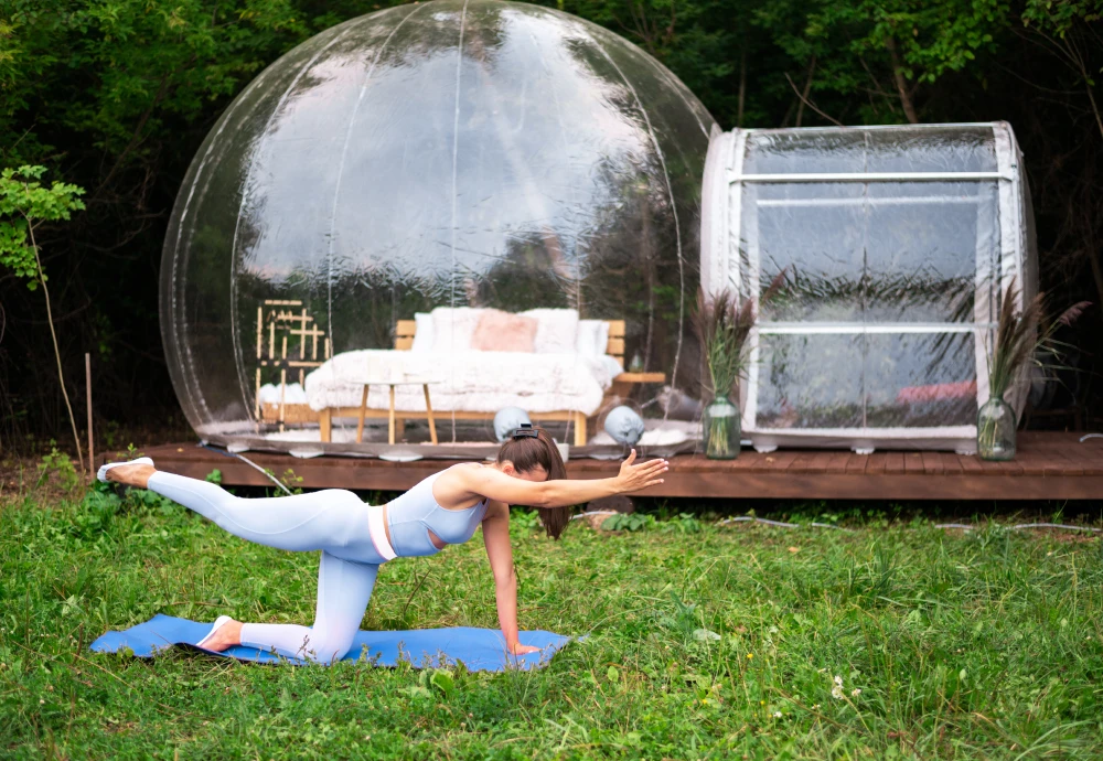Woman practicing yoga near transparent dome structure outdoors.