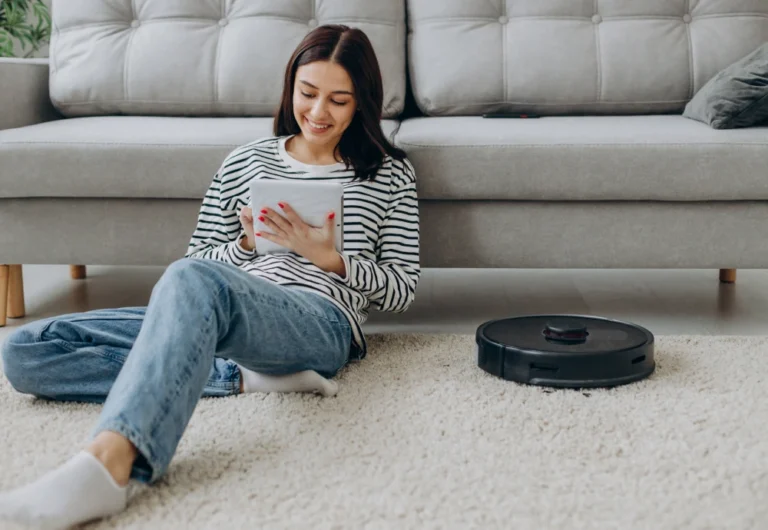 Woman using tablet while robot vacuum cleans the floor.