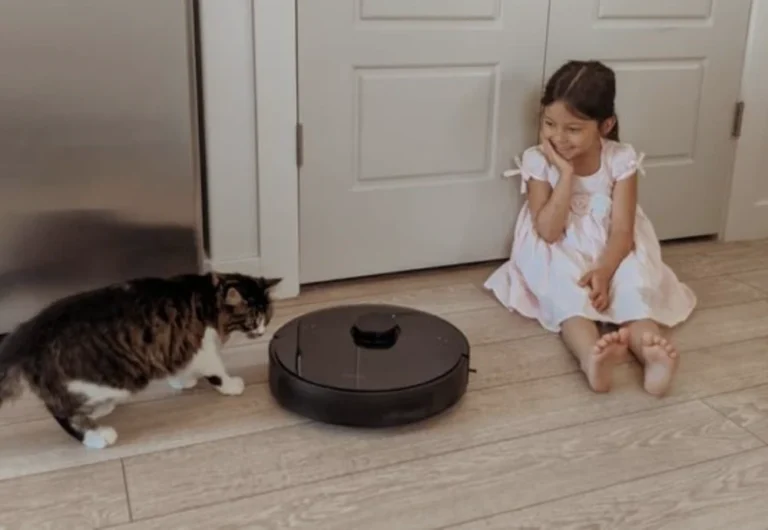 Girl and cat watching robotic vacuum cleaner.