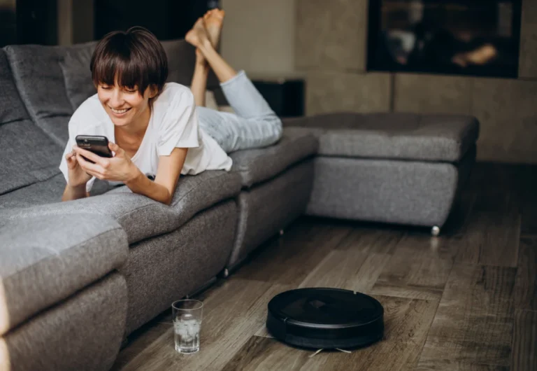 Woman smiling at phone on sofa near robotic vacuum.