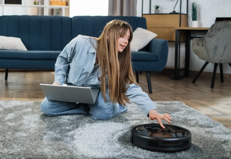 Woman using laptop programs robotic vacuum cleaner indoors.